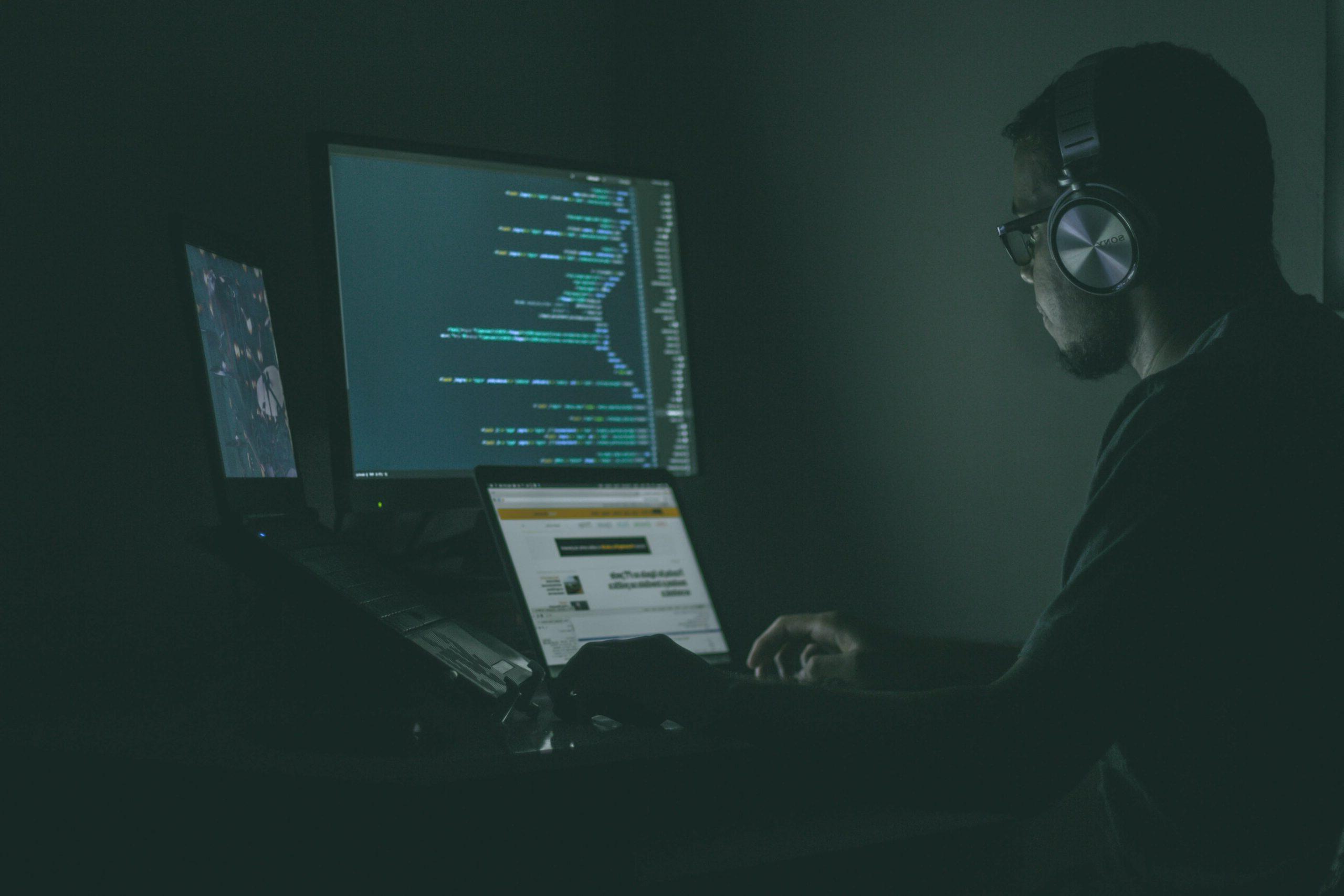 A guy coding on his computer in a dark room