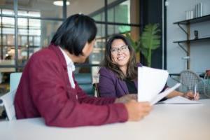 Two coworkers sitting at a desk together reviewing documents