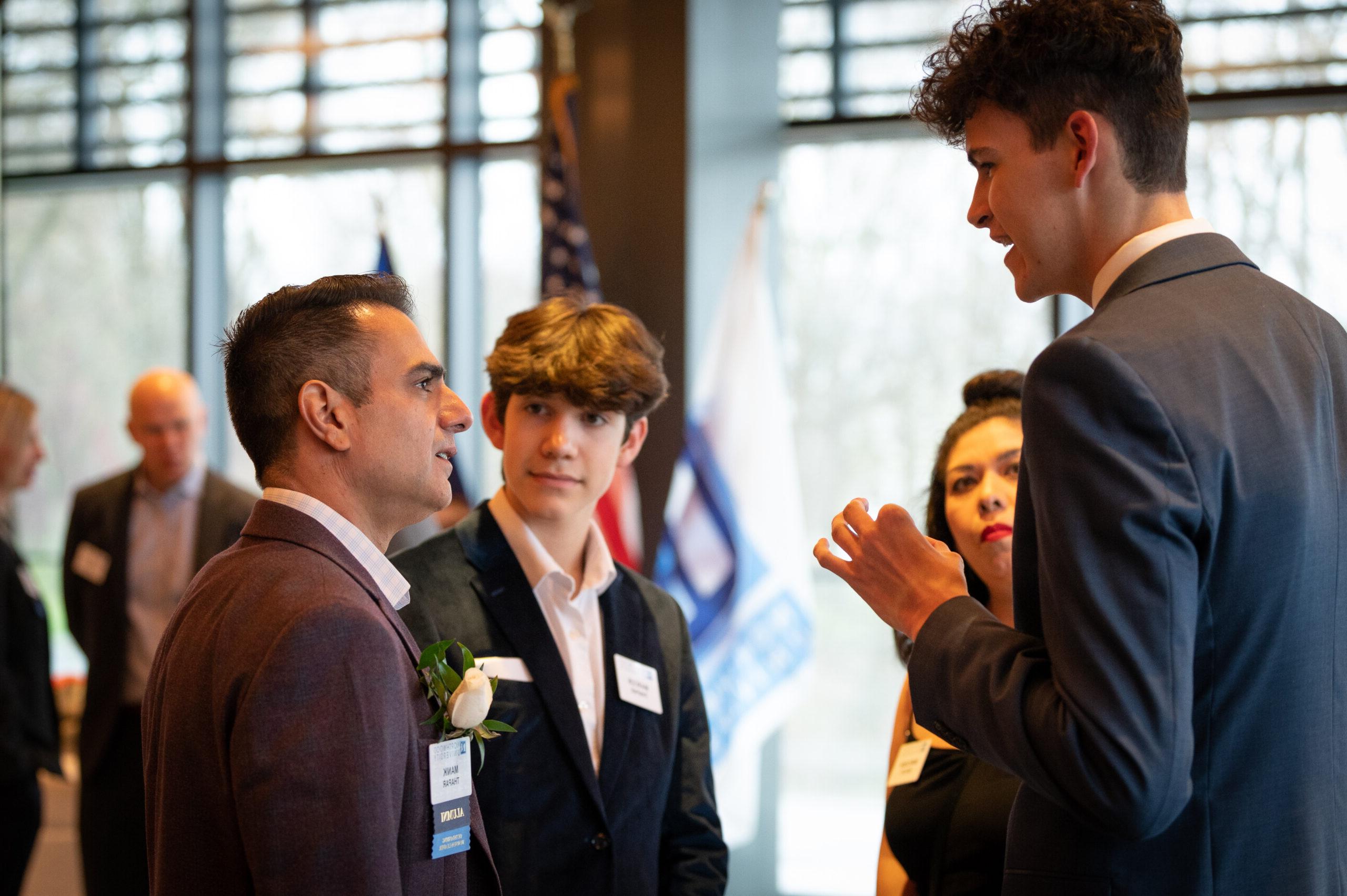 Four Northwood alumni in suits talking to each other.