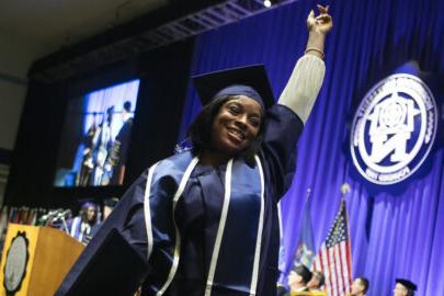 竞技宝app下载 graduate holding a fist in the air, smiling, while walking off stage with her diploma.